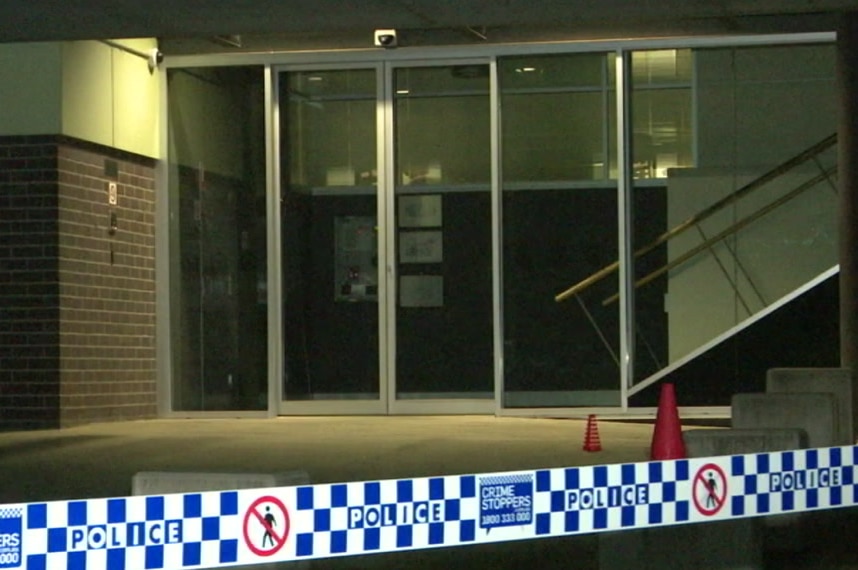 Police tape is seen with the doors of a police station in the background.