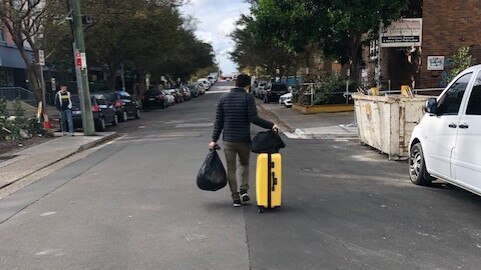 A resident of Mascot Towers walks away from the apartment block with a suitcase and bags of his belongings on June 23, 2019.