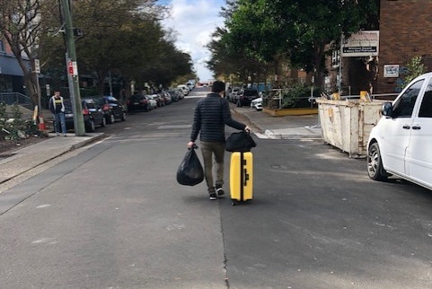 A resident of Mascot Towers walks away from the apartment block with a suitcase and bags of his belongings on June 23, 2019.