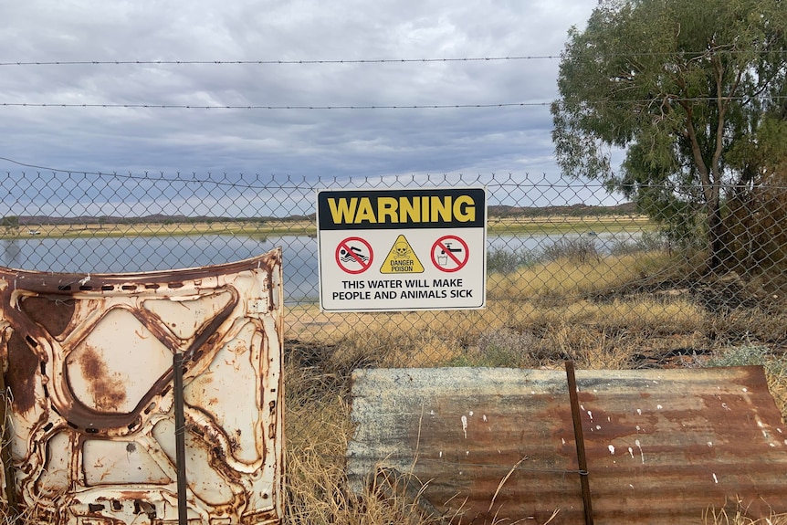 warning sign on fence reading 'this water will make people and animals sick'