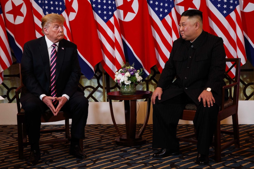 President Donald Trump seated across from North Korean leader Kim Jong Un against a backdrop of flags.
