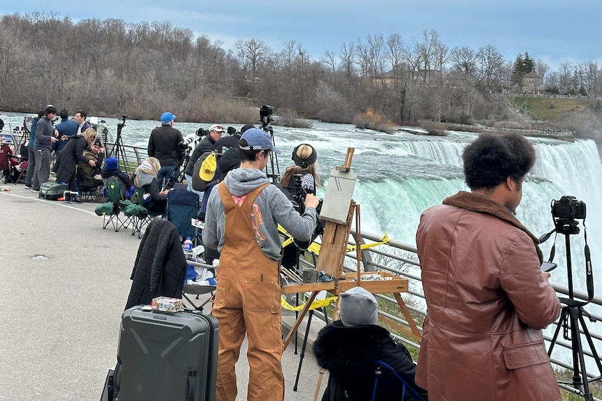 Dozens of people gather at the viewing spot near a large waterfall with cameras and tripods