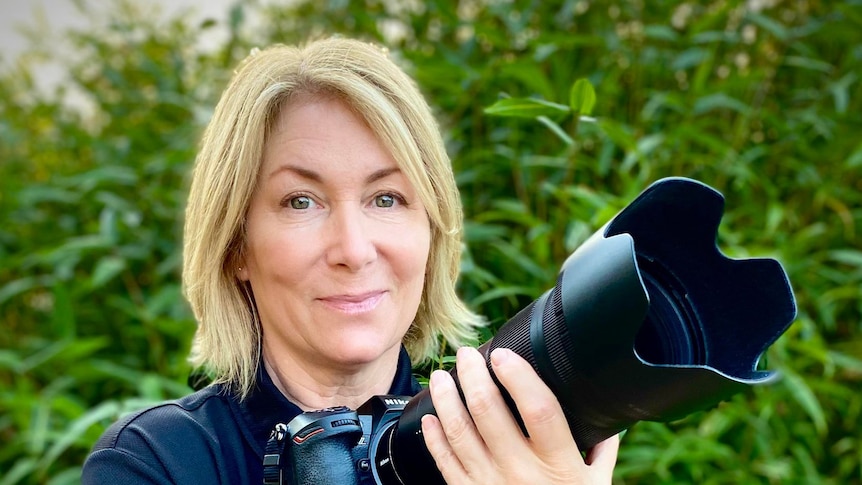 blonde woman holding a large camera and lens