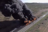 Smoke billows from the fiery wreckage of a crashed petrol tanker on the side of an outback highway