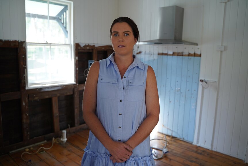 A woman in a blue dress standing in a stripped back room.