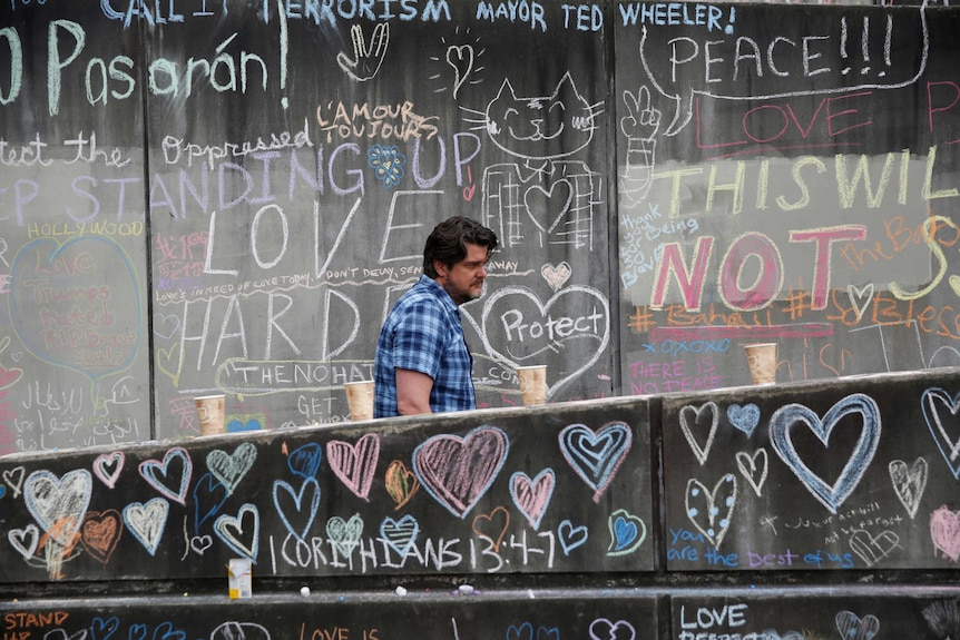 A man walks through a makeshift memorial, featuring positive words written in coloured chalk, for two men who were killed.