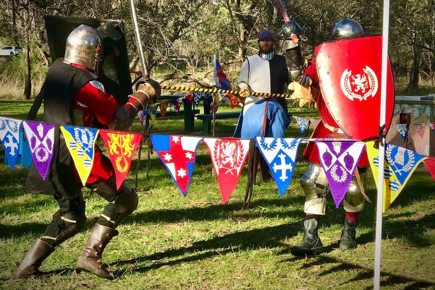 Two re-enactors in medieval armour fighting.