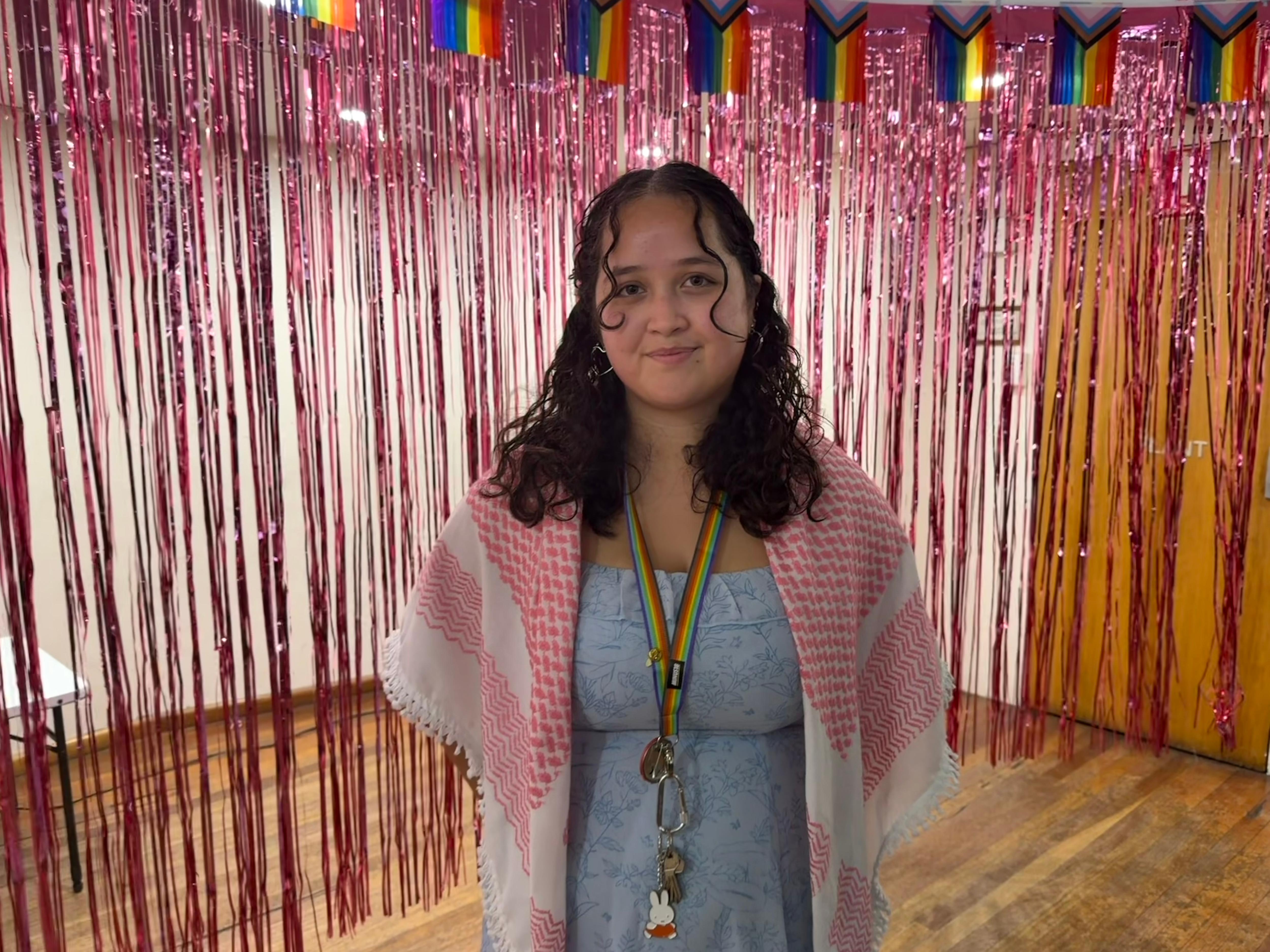 Kayla Hill com keffiyeh vermelho e renda arco-íris em um fundo de ouropel