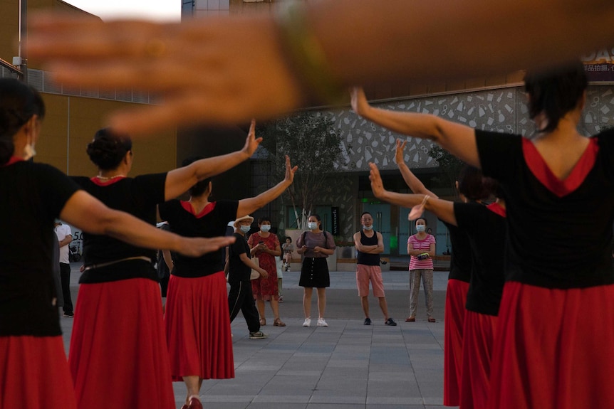 Some dancers wearing black t-shirt and red dress doing square-dancing in public in Beijing