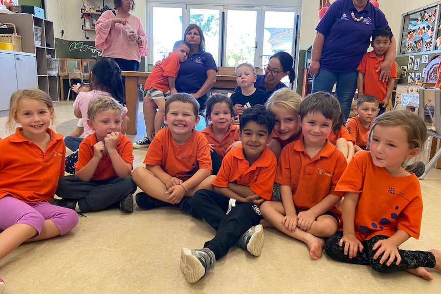 A group of young children sitting on the floor wearing red uniforms.