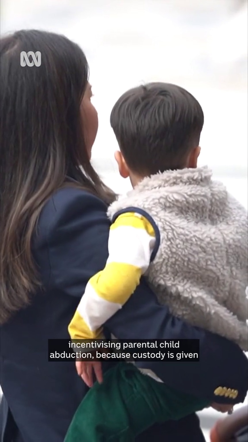 Asian woman with long black hair holding child — shown from behind