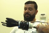 A man with a dark beard works a black robotic arm