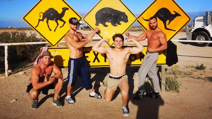 Shirtless men standing in front of animal signage.
