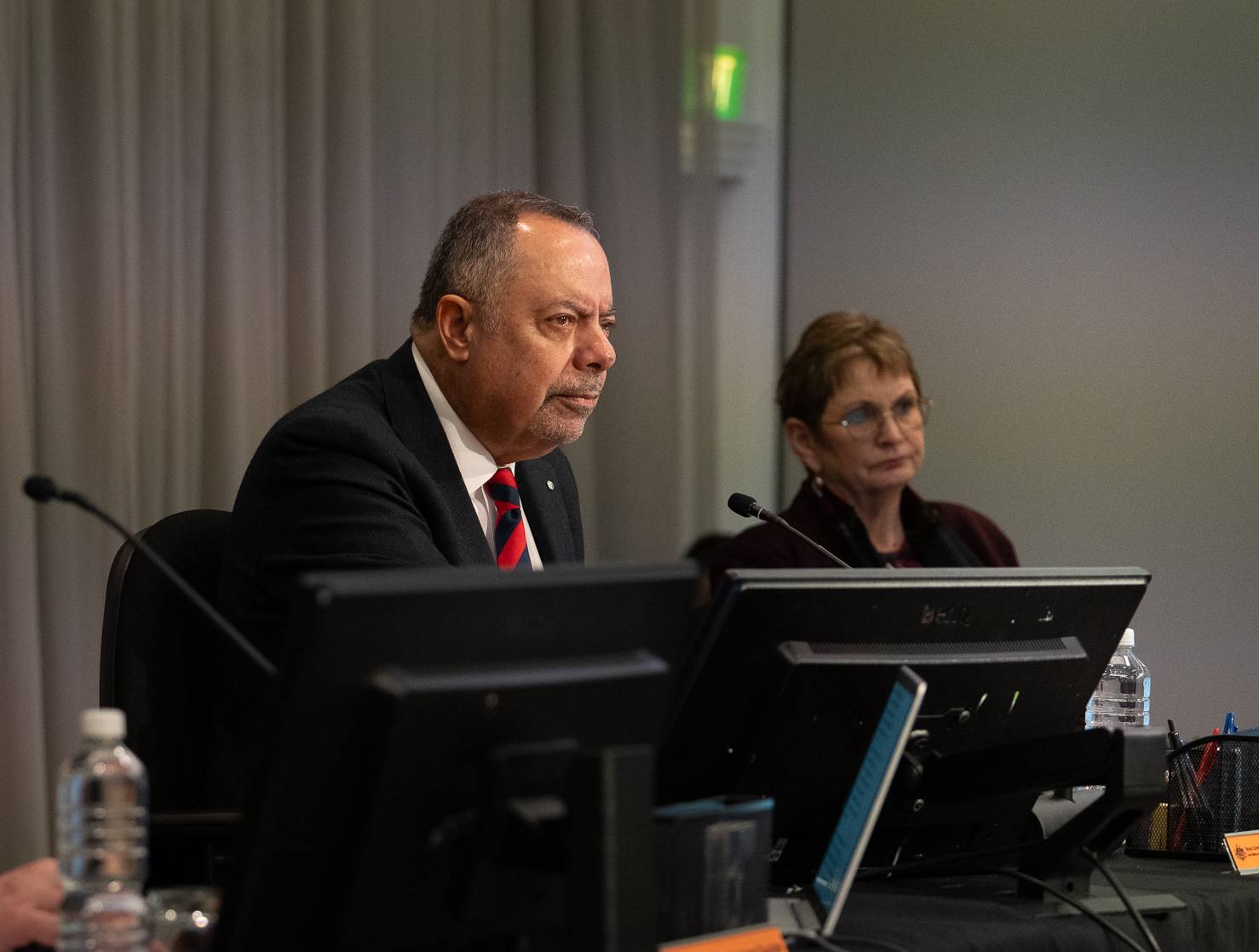 Two people sit in front of computers and microphones.