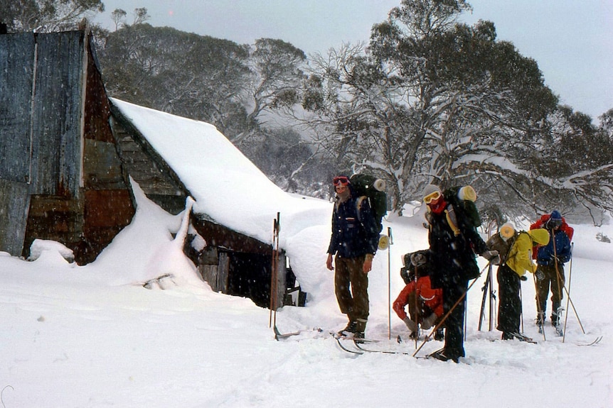 A hut in the snow with skiiers outside.