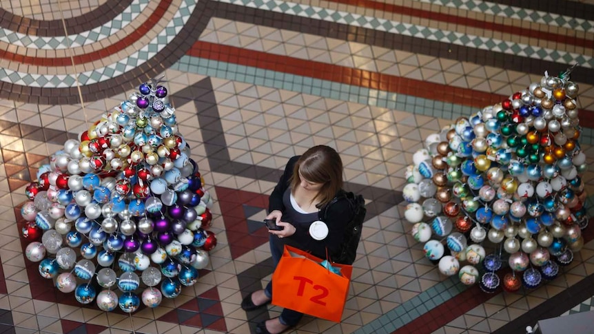 A shopper stands next to Christmas trees in the Queen Victoria Building in Sydney