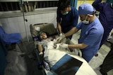 Doctors attend to a young girl laying on a hospital bed with injuries.