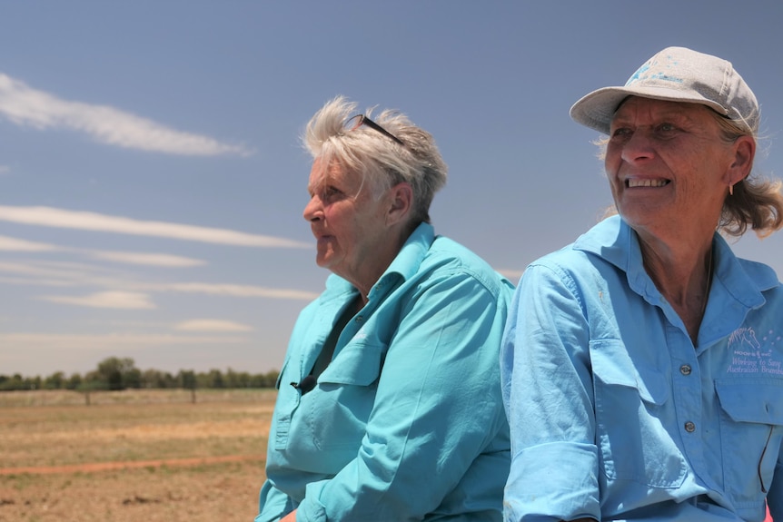 Two women sit and look at bare paddocks under a blue sky