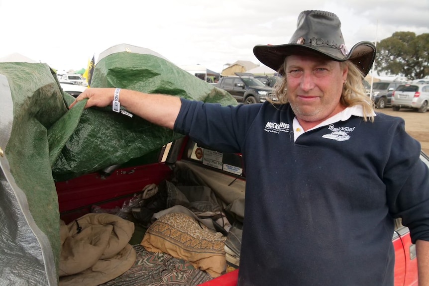 A man in a leather cowboy hat stands at the rear of a ute