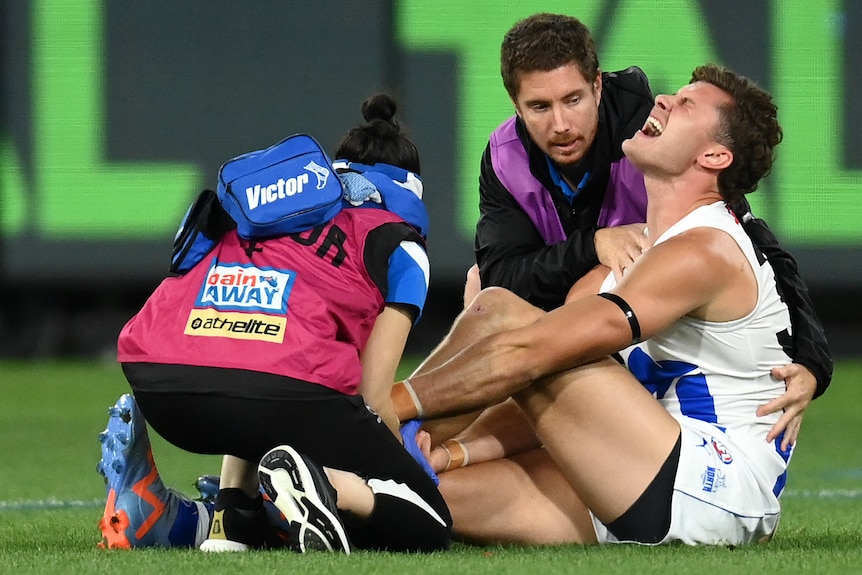 A North Melbourne Kangaroos AFL player grimaces as he is attended to do during a match against the Melbourne Demons.