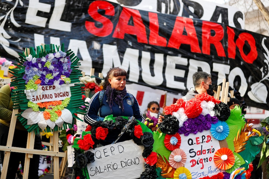 Two people holding brightly coloured banners which said "QEPD Salario Digno"