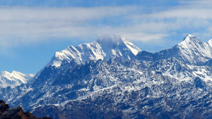 Clouds obscure the top of a large snow-capped mountain.