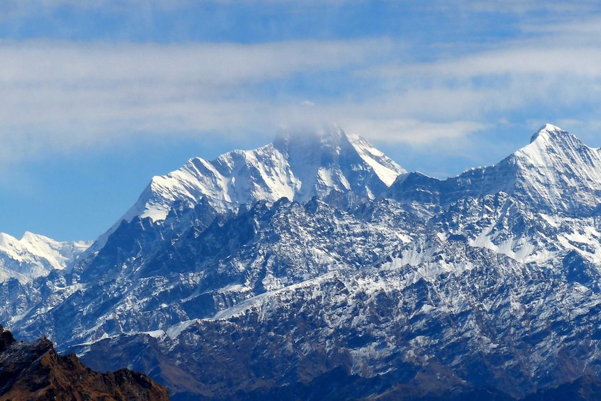 Clouds obscure the top of a large snow-capped mountain.