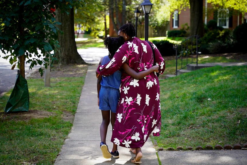A mother and daughter walking arm in arm down a suburban street