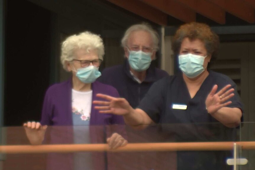 three people in surgical masks overlooking a balcony, one woman has animated hands