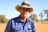 Man in drill shirt and broad-brimmed hat with background of red dirt and blue sky.