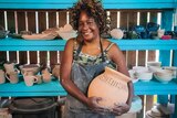 A woman smiles as she holds a big ceramic vase.