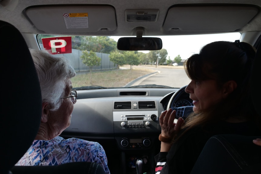 Two woman sit in the front seats of a car talking, preparing to drive.