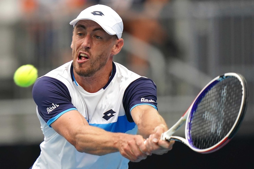 A male tennis player watches the ball as he stretches for a double-fisted backhand at the Australian Open.