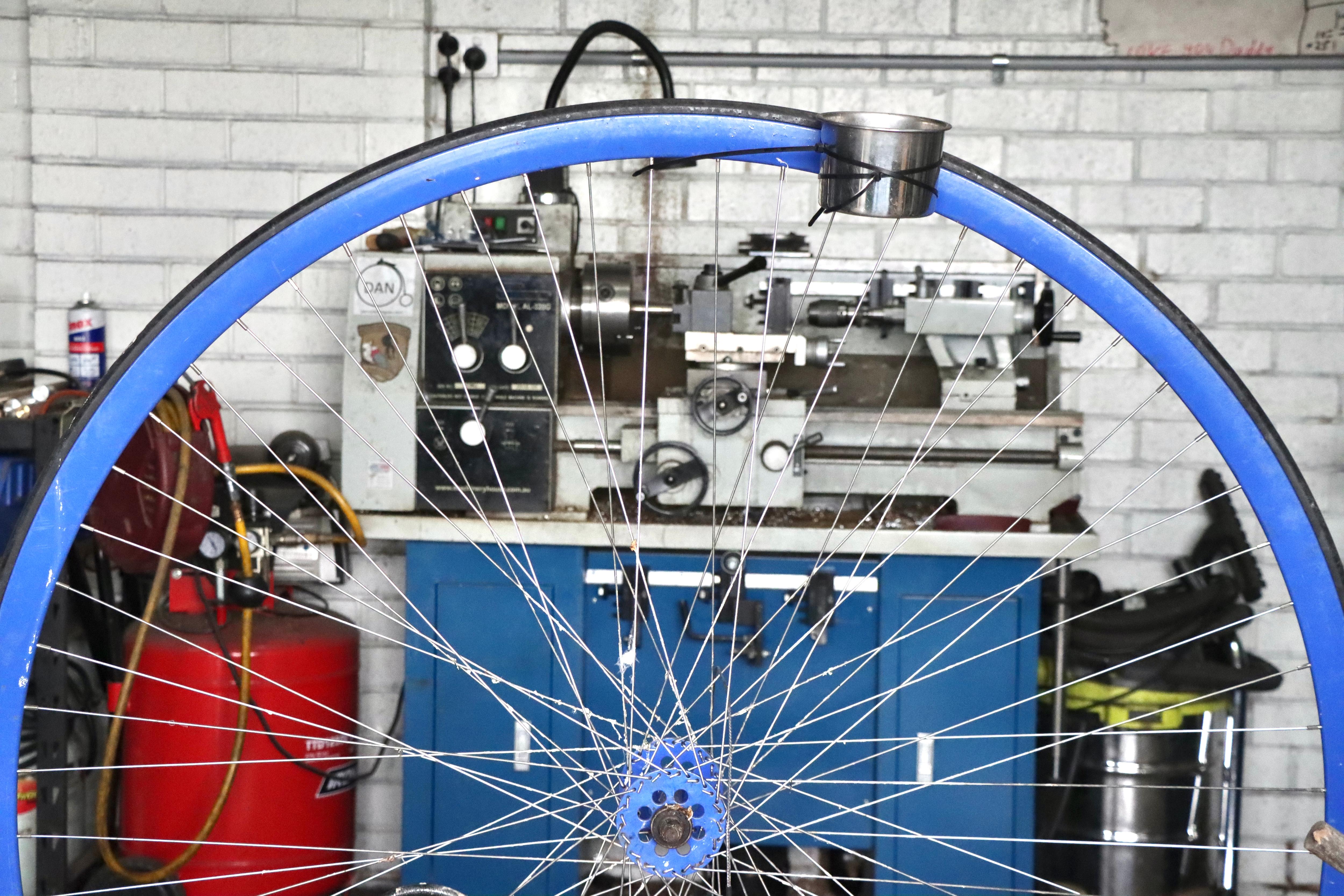A close up of one of a blue penny farthing wheel, a blue cabinet behind with tools.