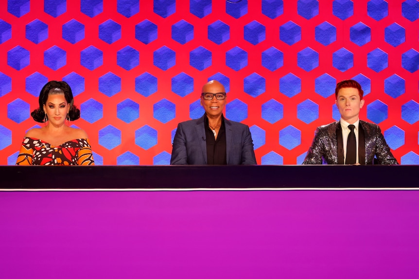 RuPaul's Drag Race Down Under judges Michelle Visage, RuPaul Charles and Rhys Nicholson sitting at the judging panel