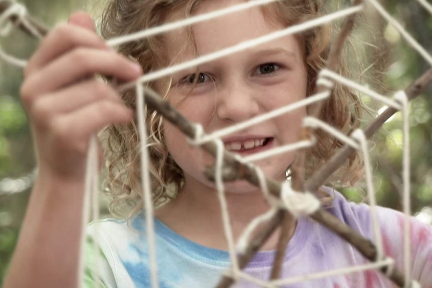 Girl looking at a web made of sticks and twine
