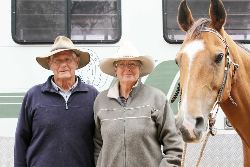 A man and a woman standing in front of a caravan holding one of their horses.