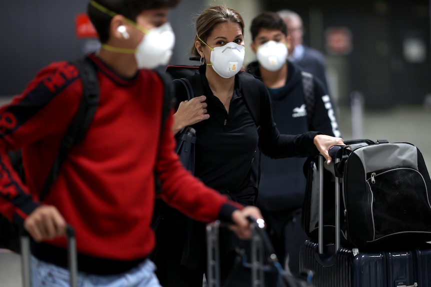Woman queues behind a young man at an airport, both wearing face masks.