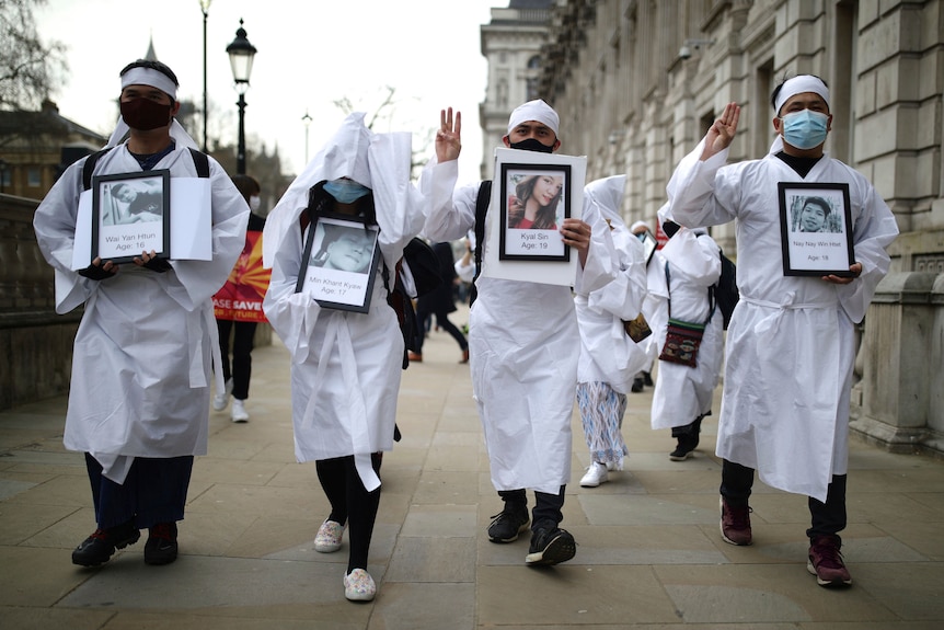 Protesters holding photos of protestors killed wear white cloaks and bandanas as they march in Westminster.