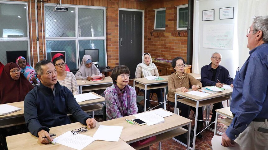 People sit at desks in an English class being taught at a refugee and migrant service.