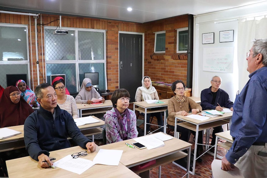 People sit at desks in an English class being taught at a refugee and migrant service.