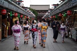 A group of women in Japanese traditional wear walk past two women in face masks in an ornate temple.