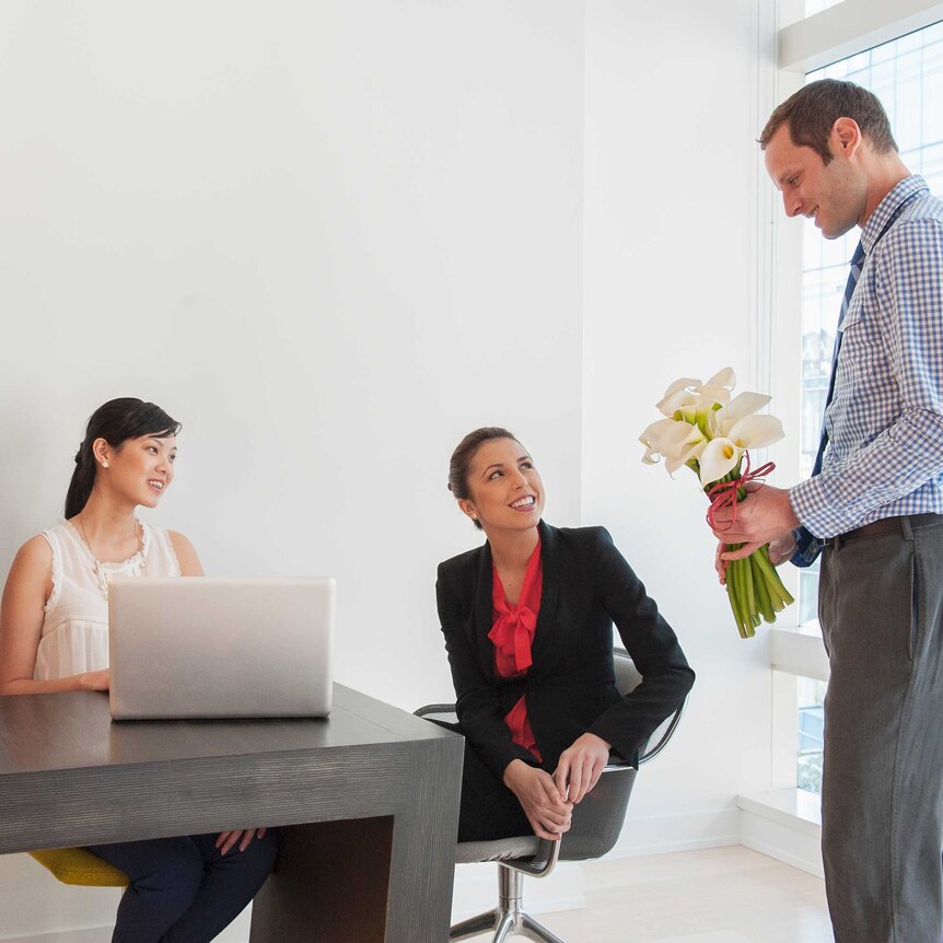 A man giving flowers to a woman in a meeting room, they are flanked by two other women.