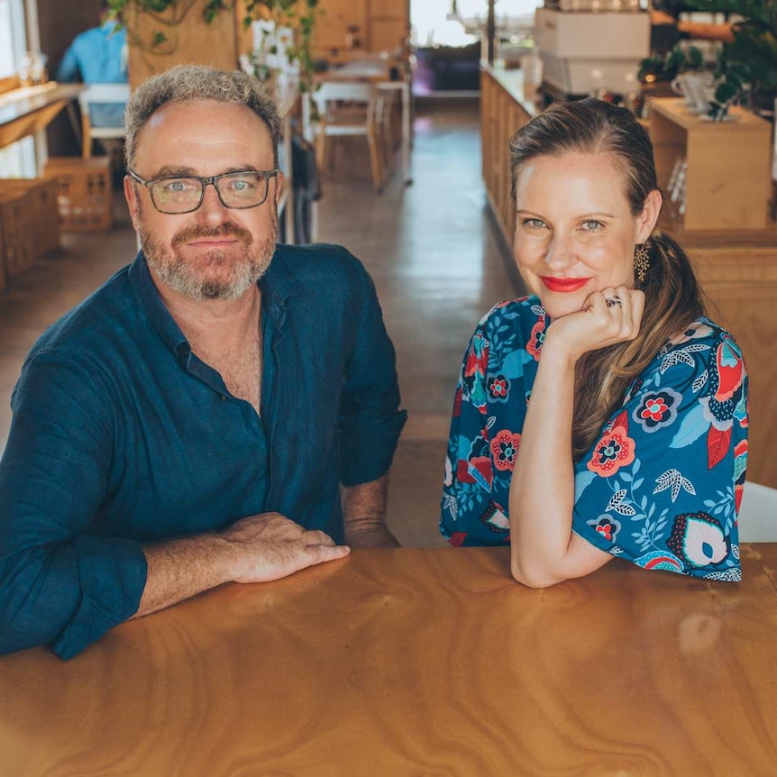 A man with curly grey hair and a beard, and a woman with long, dark blonde hair, sitting in a cafe.