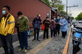 Group of various people in a queue outside on Beijing street with masks on