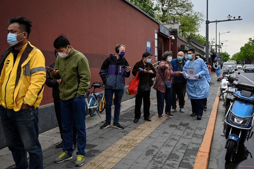 Группа разных людей в очереди на улице Пекина в масках.