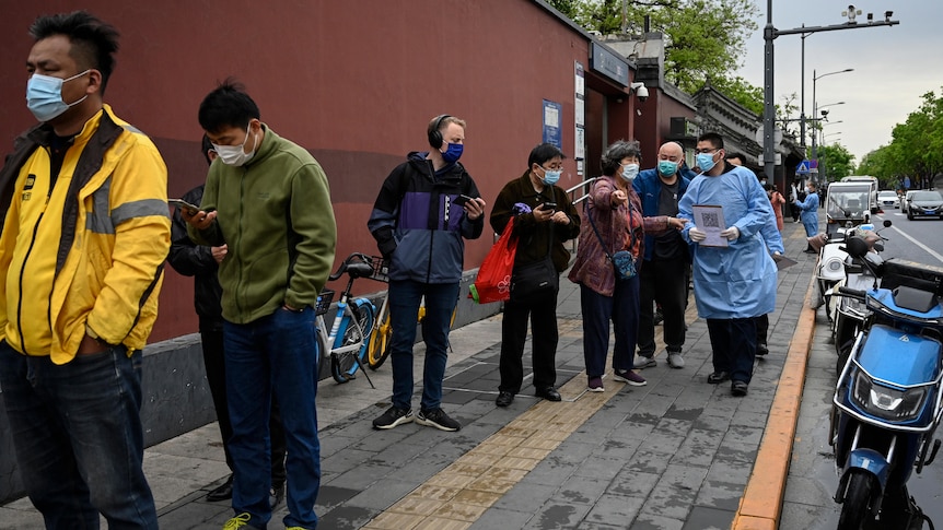 Group of various people in a queue outside on Beijing street with masks on