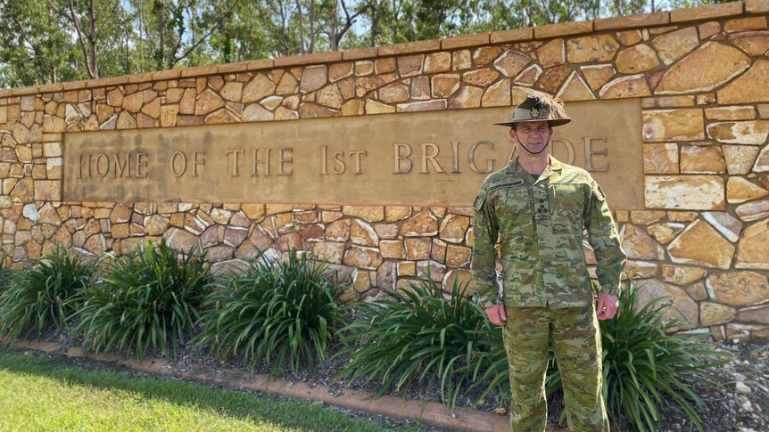 Brigadier Ashley Collingburn stands against a sign which reads 'Home of the 1st Brigade'.