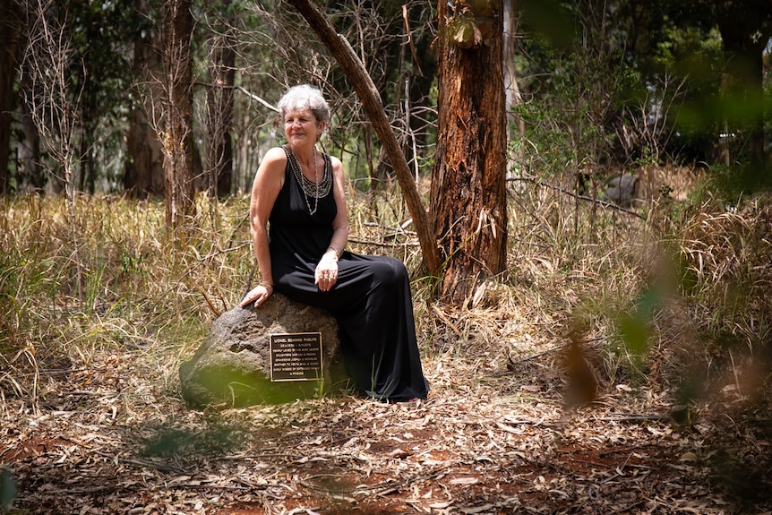 Woman sits on headstone in bushland cemetery, pictured in story about eco friendly funerals and burials.