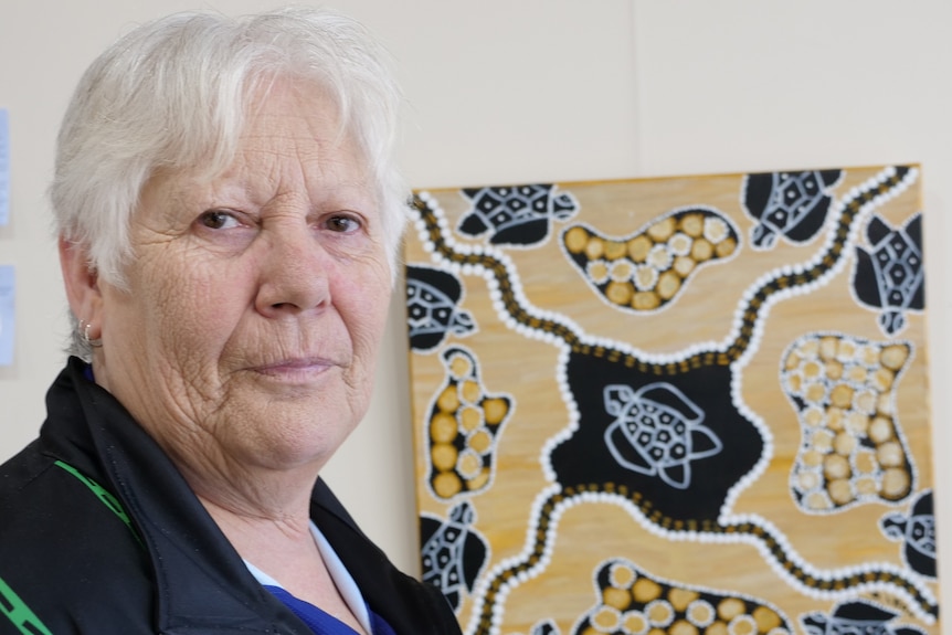 Woman stands in front of Indigenous painting 